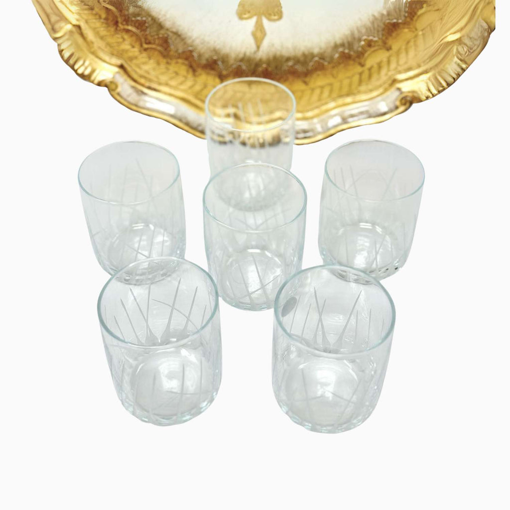 Set of six clear glass tumblers with a gold decorative plate in the background