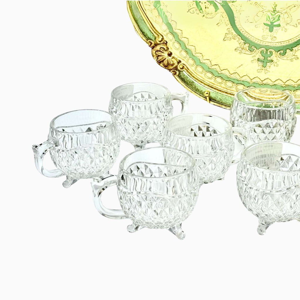 Set of clear glass tea cups with a decorative gold and green plate in the background.