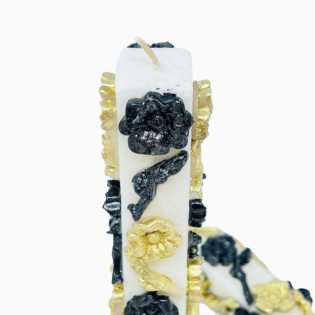 Decorative candle with black and gold floral designs on a white background