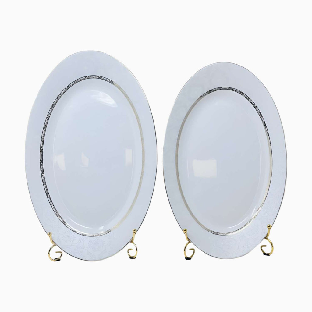 Two oval white plates with gold rims on a white background