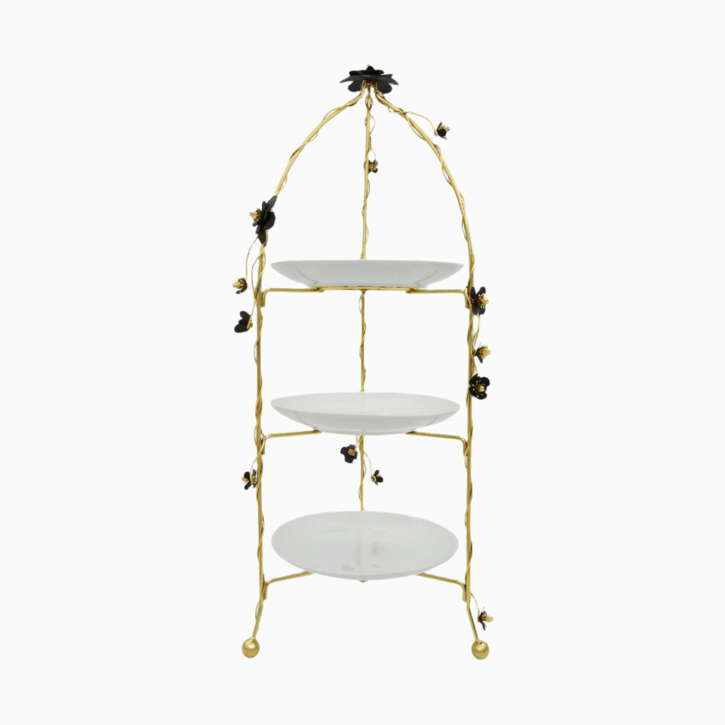 A three-tier round serving platter with a brass frame and white porcelain plates, decorated with small gold-colored beads or accents.