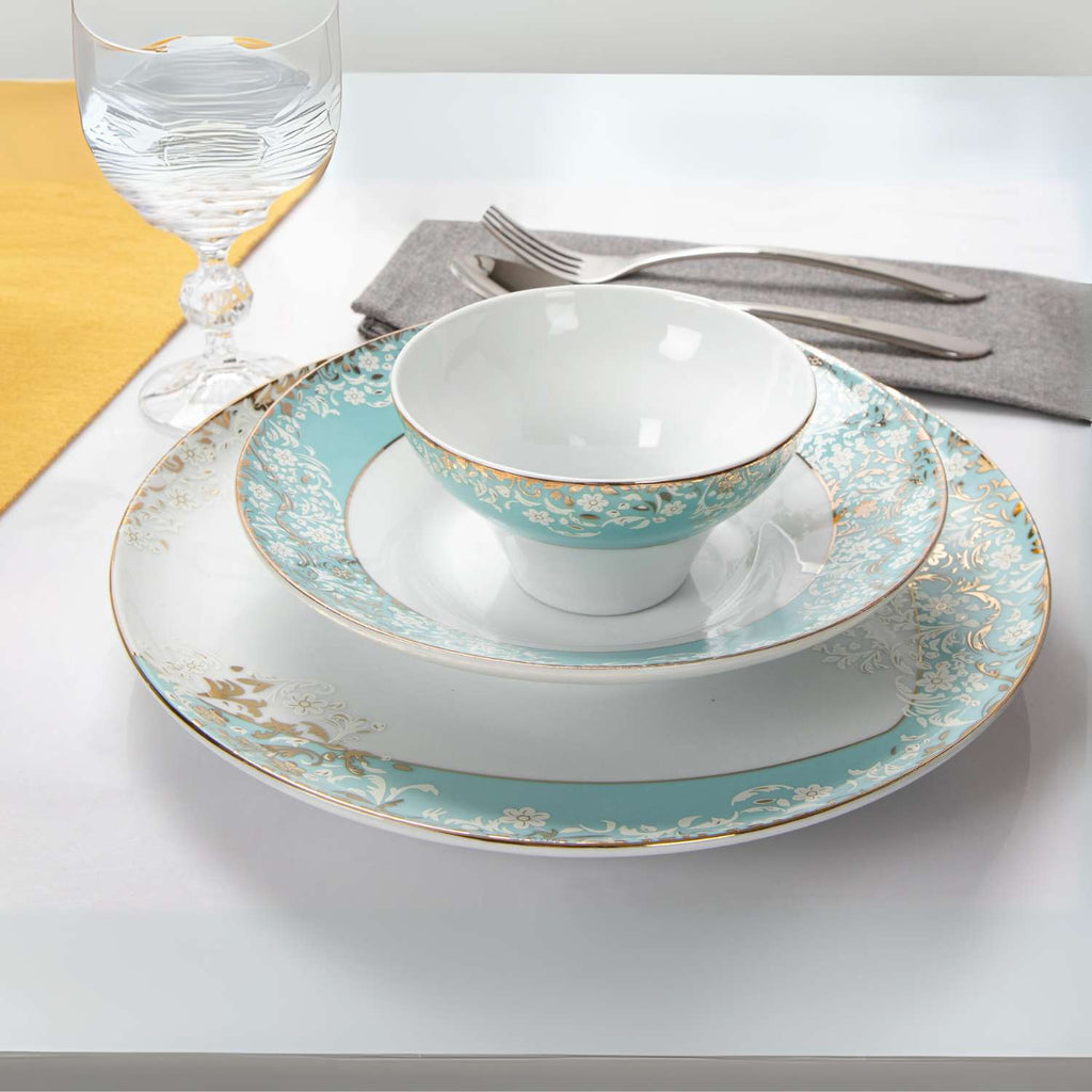 Teal and gold ceramic dinnerware set on a white table with a glass of water and yellow napkin.