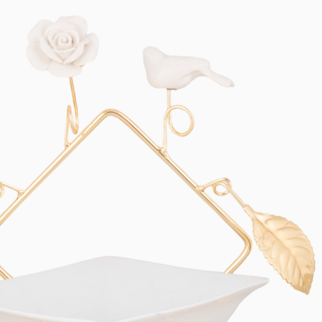 A white porcelain snack bowl on a golden tone stand, featuring floral and bird designs as decorations.