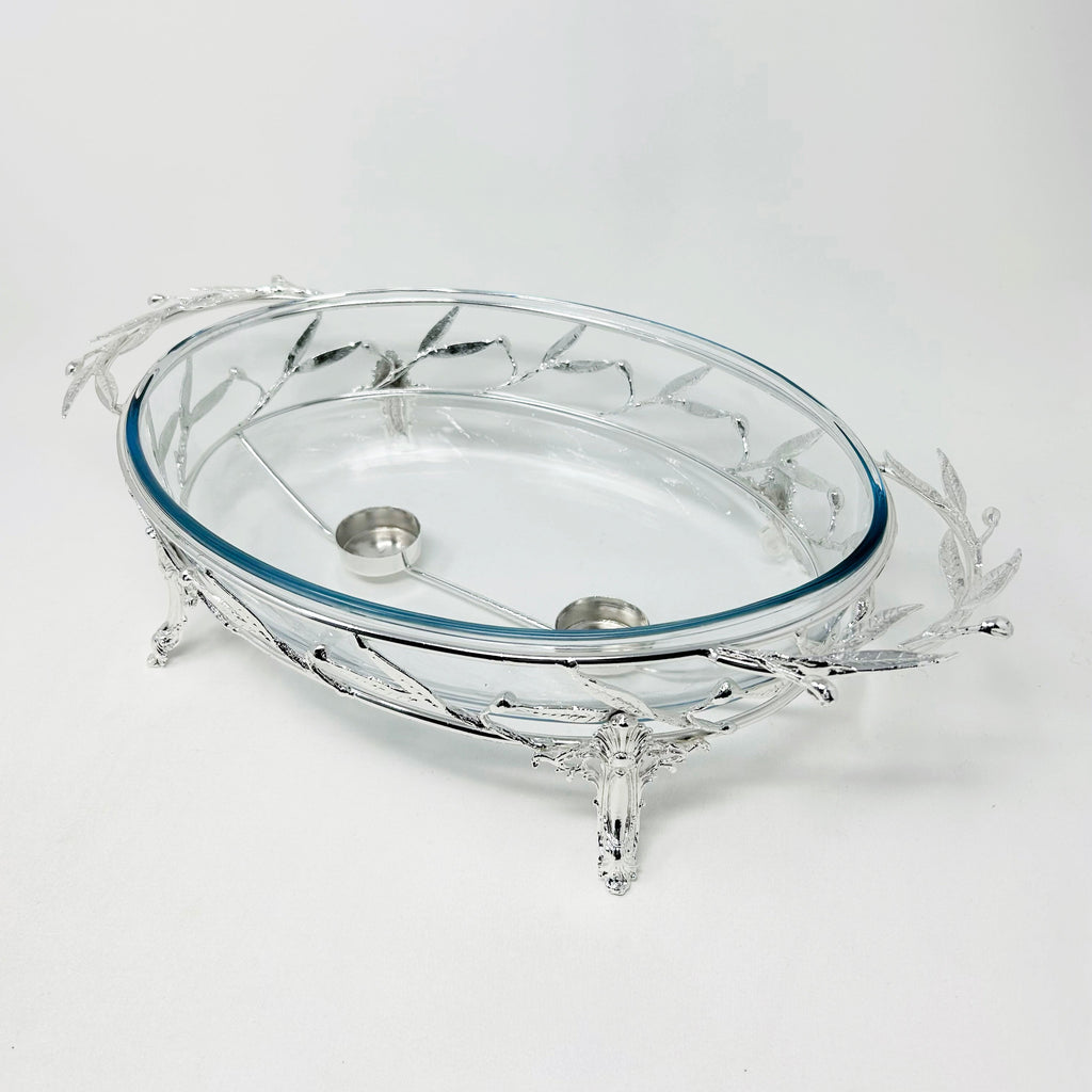 Elegant oval glass Pyrex serving dish set in an intricately crafted silver-tone metal stand featuring detailed leaf motifs and sculpted legs. Noble Home Gifts